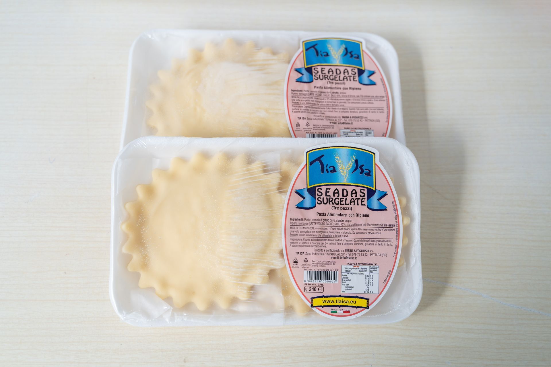 Ravioli confezionati in una vaschetta bianca con due ravioli crudi su uno sfondo di stoffa