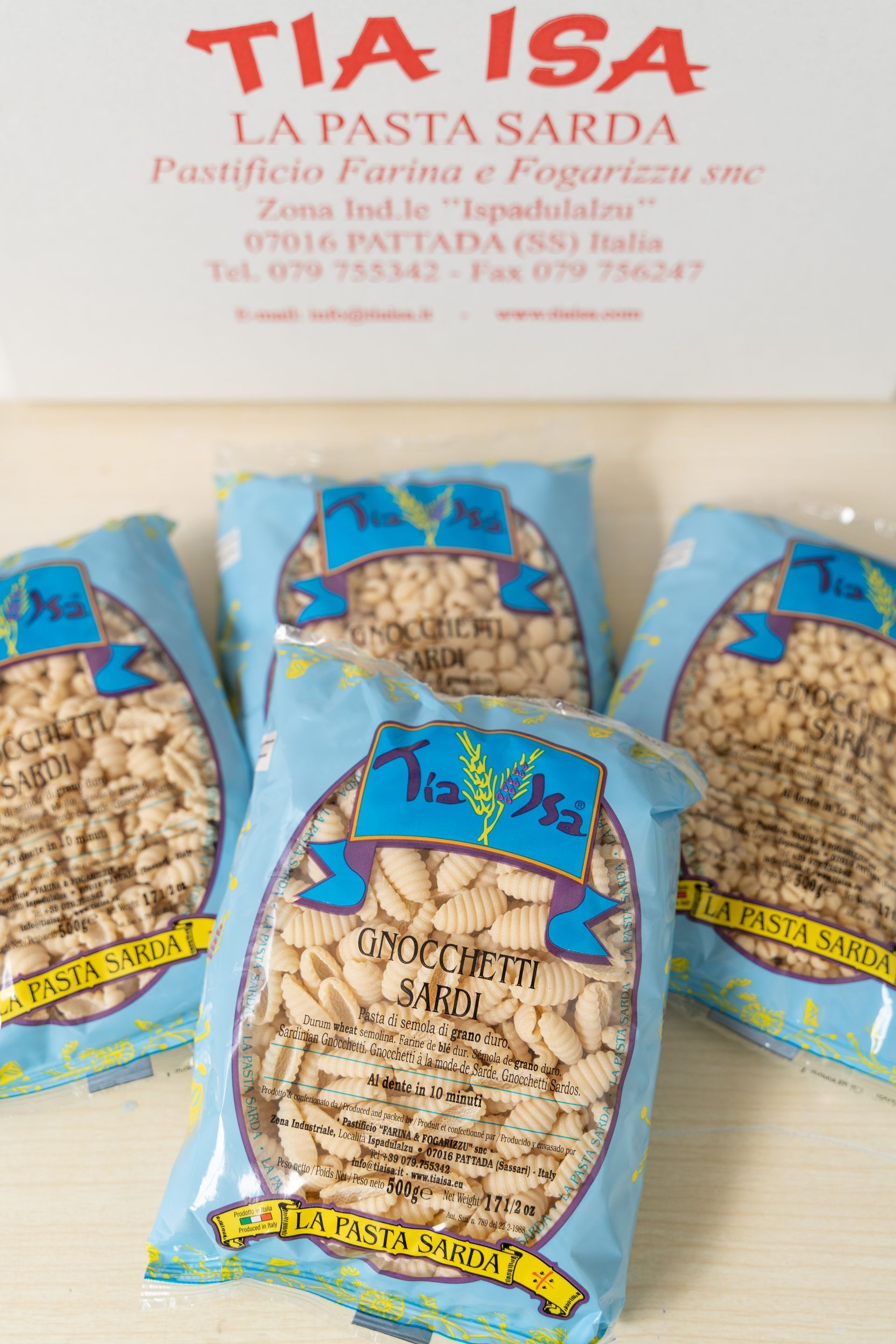 Sacchetti assortiti di pasta blu davanti all’insegna rossa e bianca della panetteria “TIA ISA”