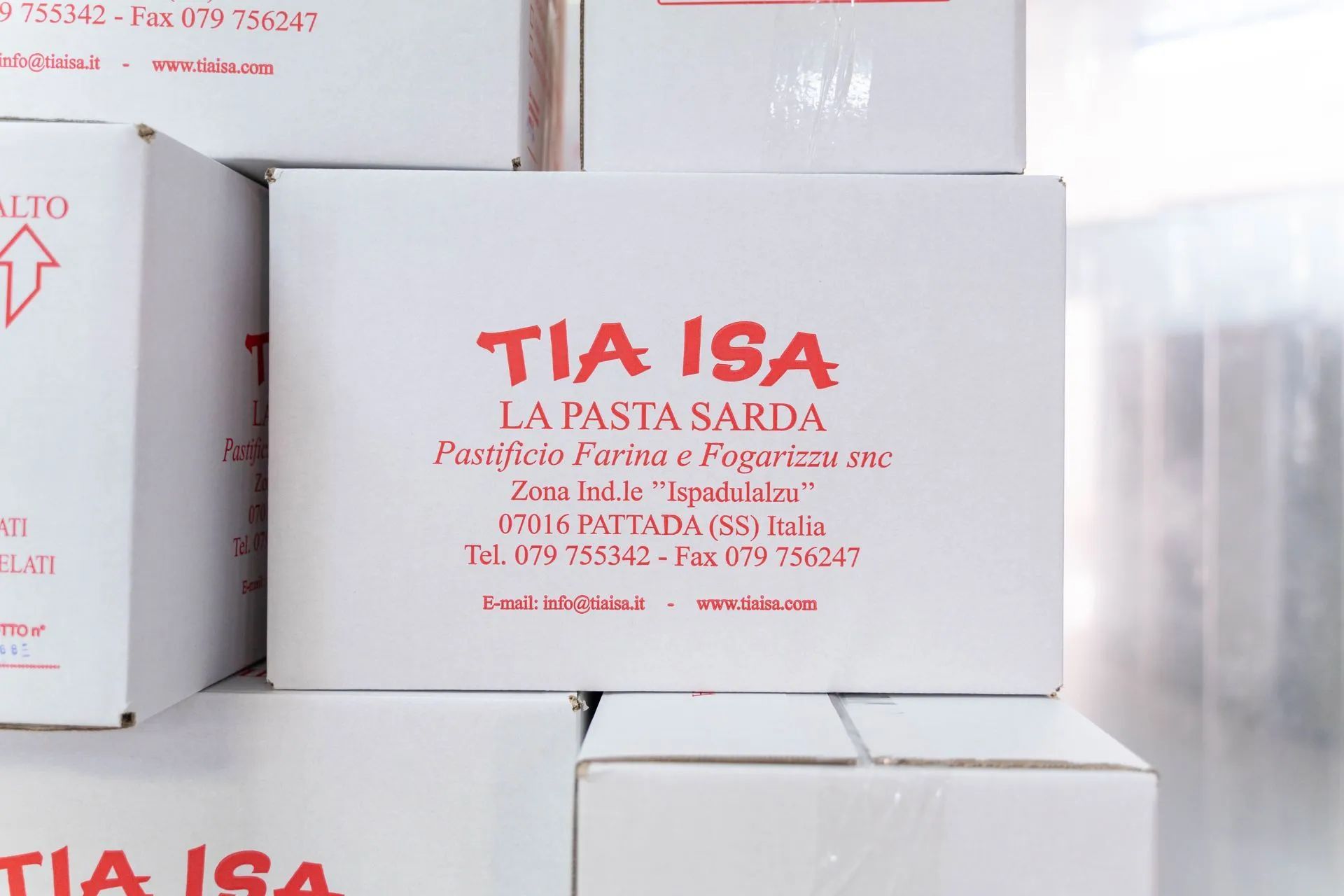 Scatole di cartone bianche impilate, con la scritta rossa “TIA ISA” e “PASTA SARDA”.