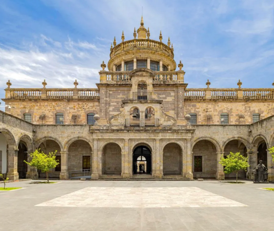 Edificio histórico de piedra ornamentado con arcos, detalles dorados y una cúpula central bajo un cielo azul.