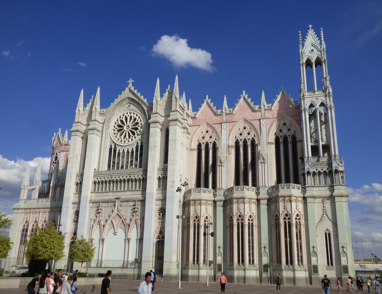 Fachada de una catedral gótica bajo un cielo azul, con algunas personas en la plaza de abajo.