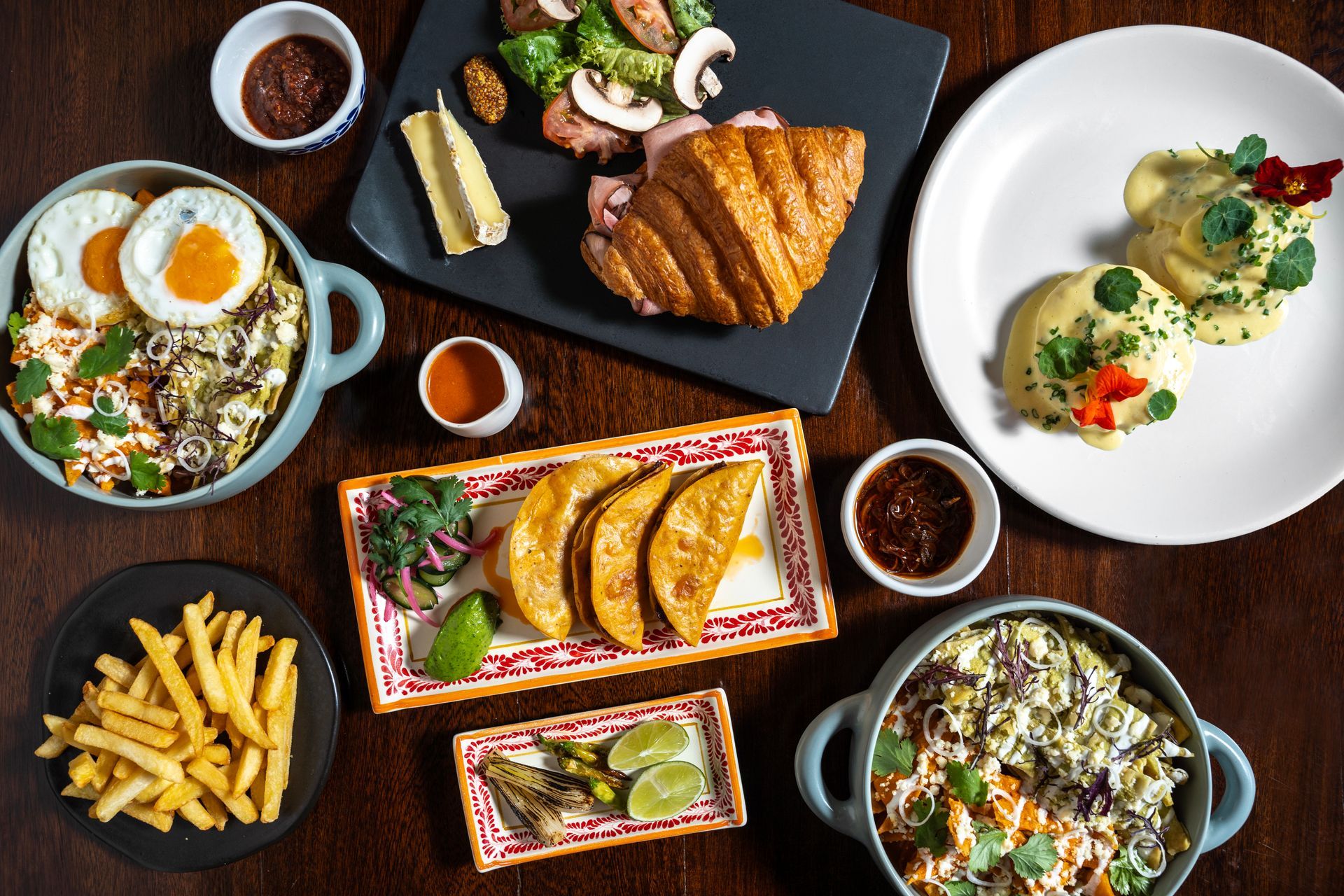 Variedad de platos gourmet sobre una mesa de madera oscura, que incluyen pasta, patatas fritas, sándwiches y huevos.