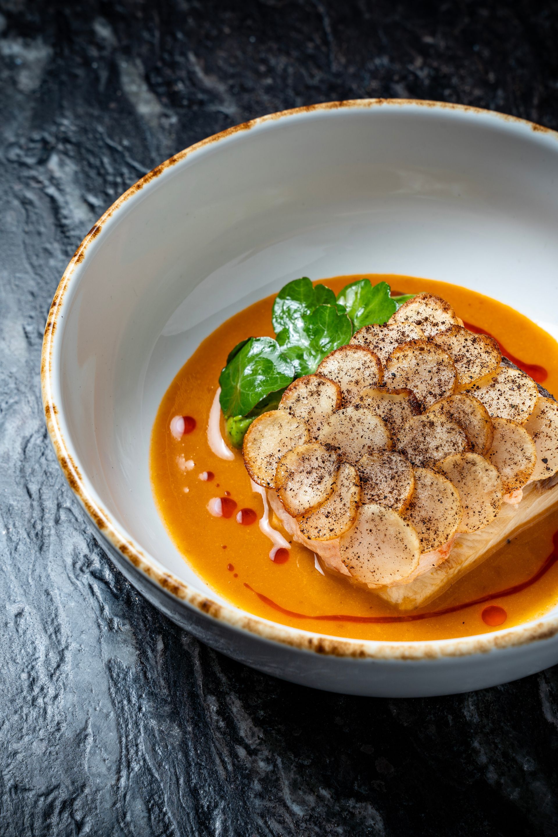 Pescado sellado al plato en salsa de naranja con hierbas sobre un tazón blanco.
