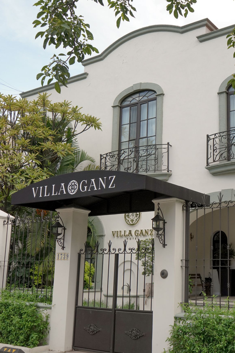Elegante entrada blanca de Villa Ganz con toldo negro, verja de hierro y pequeñas ventanas de balcón.
