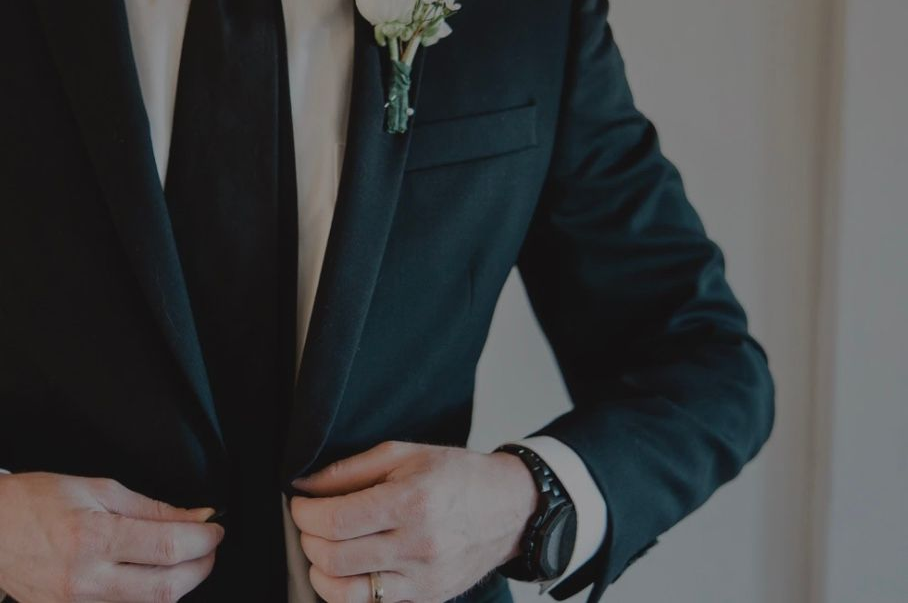 Los novios se toman de la mano, mientras el novio se abotona una chaqueta oscura.
