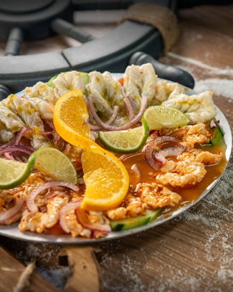 Plate of seafood ceviche, garnished with orange slices and lime wedges.