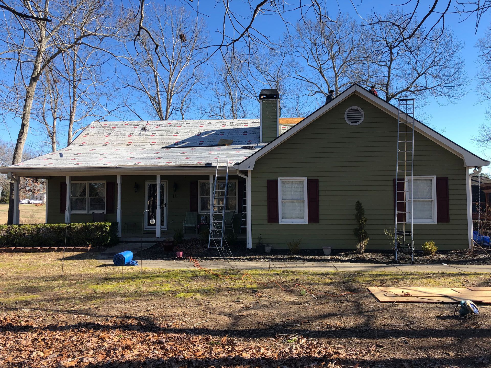 A green house with a white roof and red shutters is being remodeled.