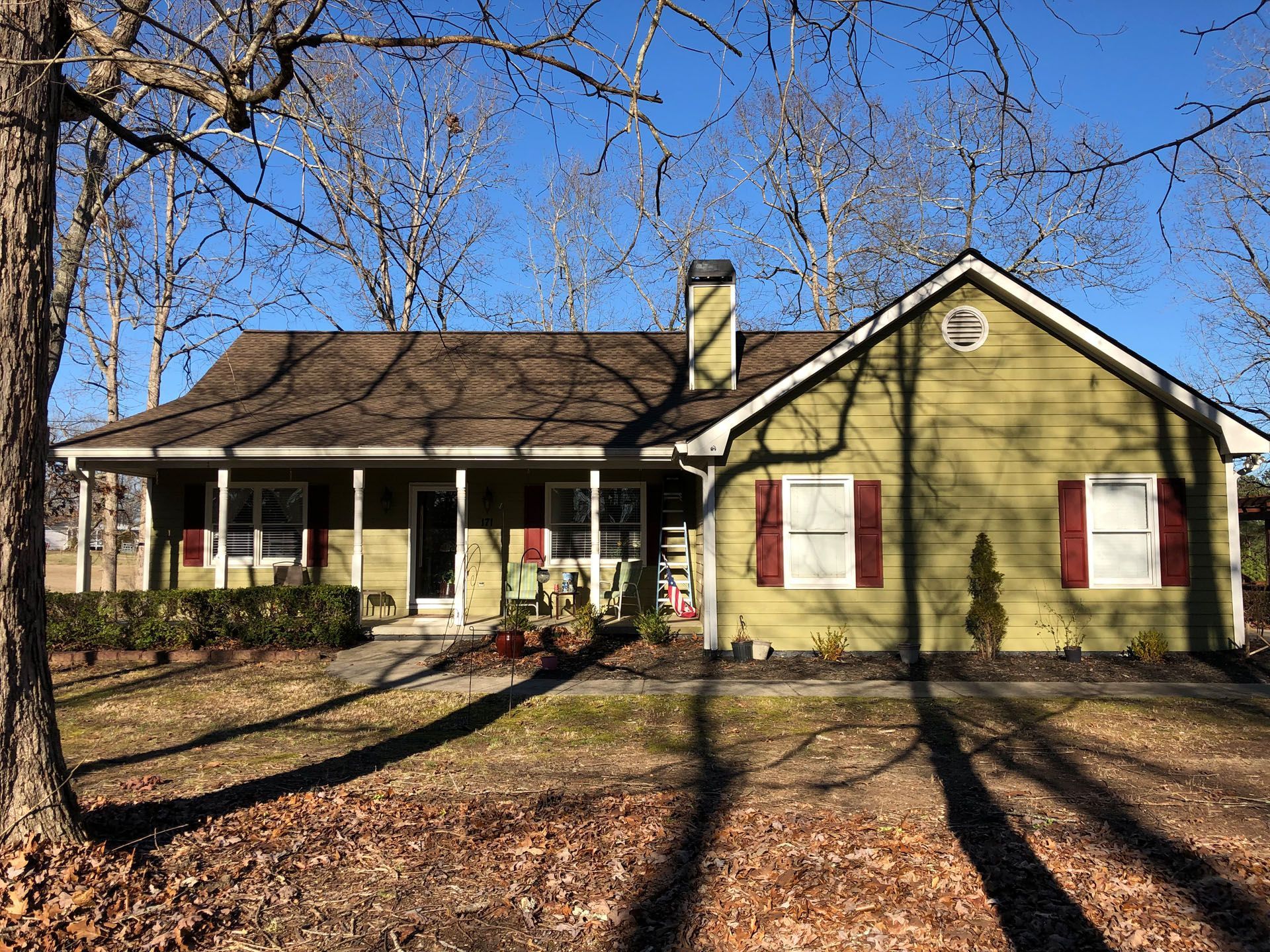 A green house with red shutters is surrounded by trees on a sunny day.
