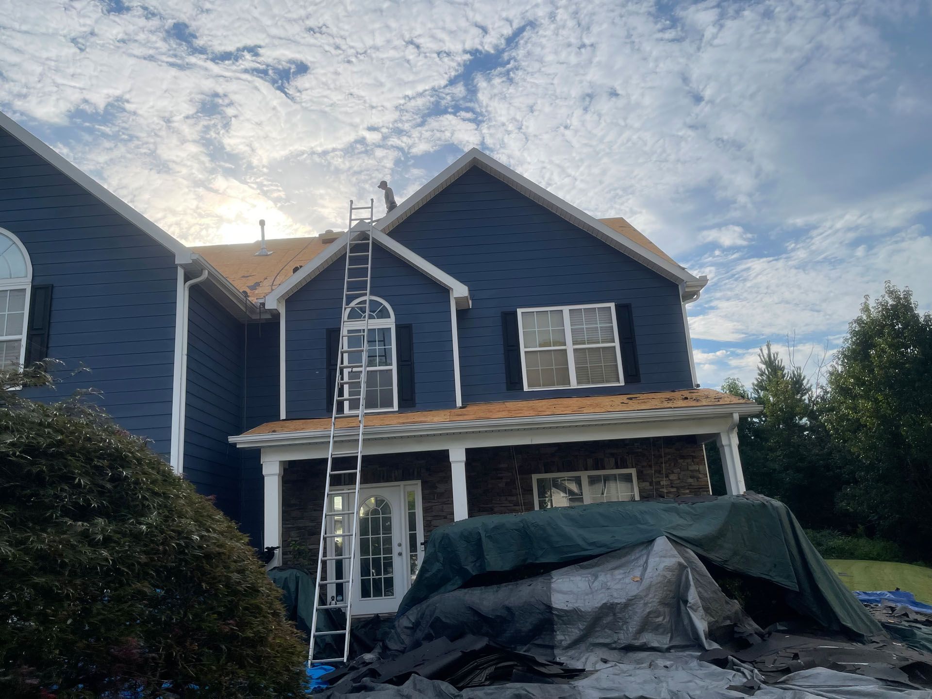 A blue house with a ladder on the roof is being painted.