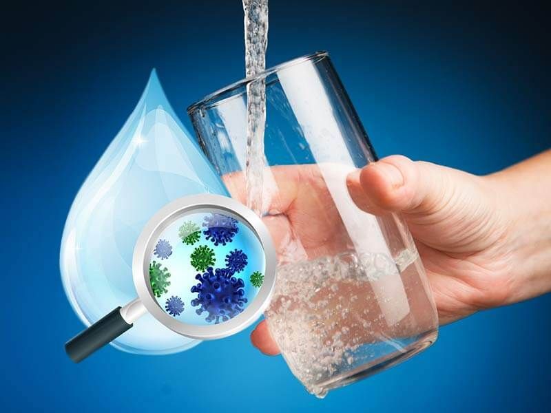 A hand is holding a glass of water with a magnifying glass showing bacteria in it.