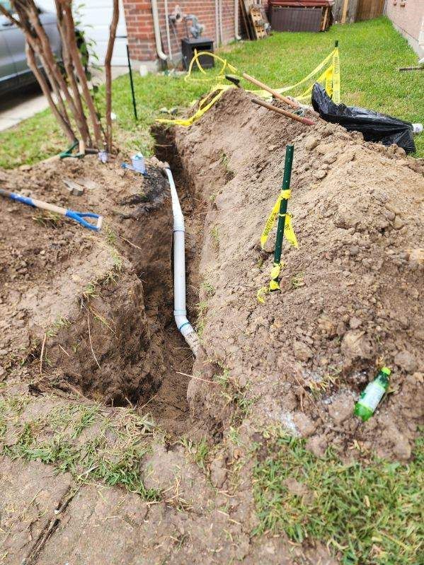 Utility trench dug in a yard with exposed pipes, caution tape, and a black tarp near a house.