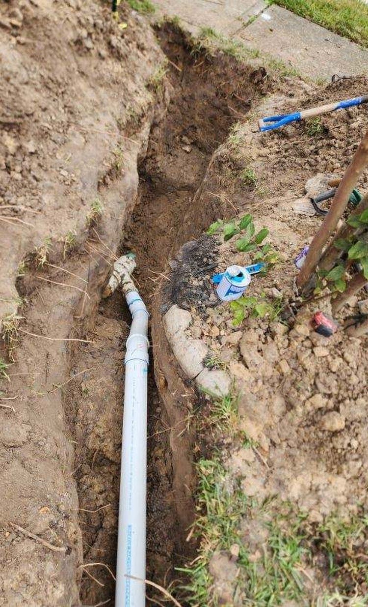 A white pipe is being installed in the dirt next to a sidewalk.