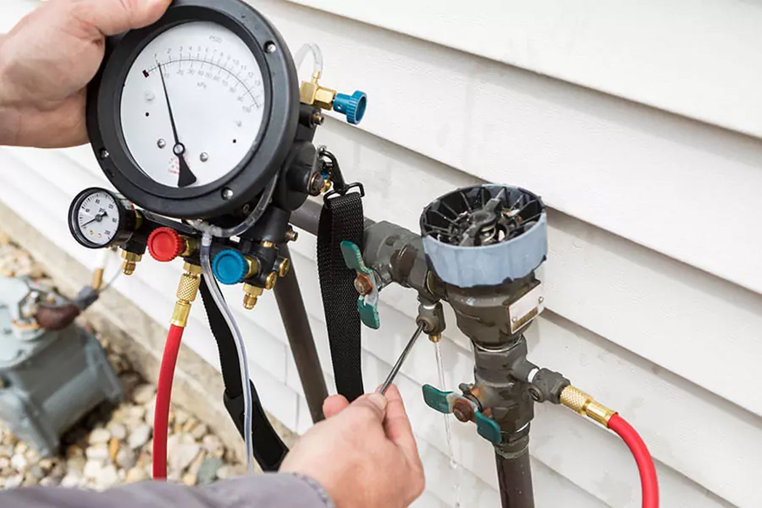 A man is holding a pressure gauge next to a pipe.