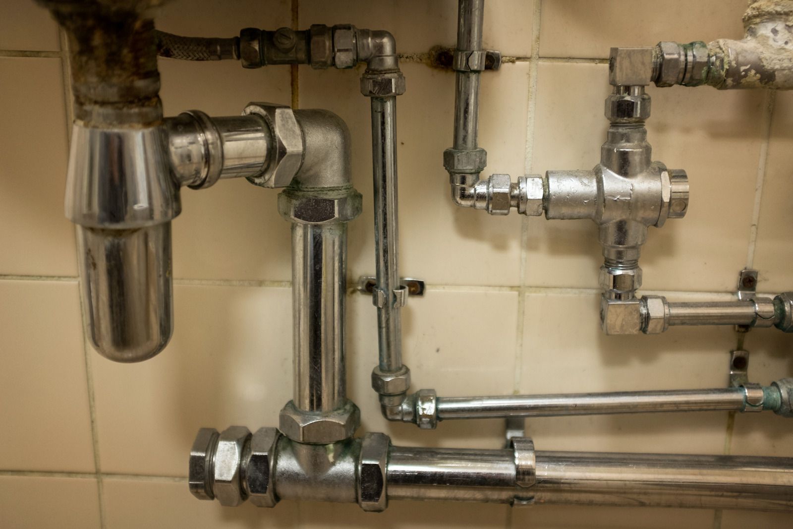 Shiny metal plumbing pipes and fittings mounted against a beige tiled wall