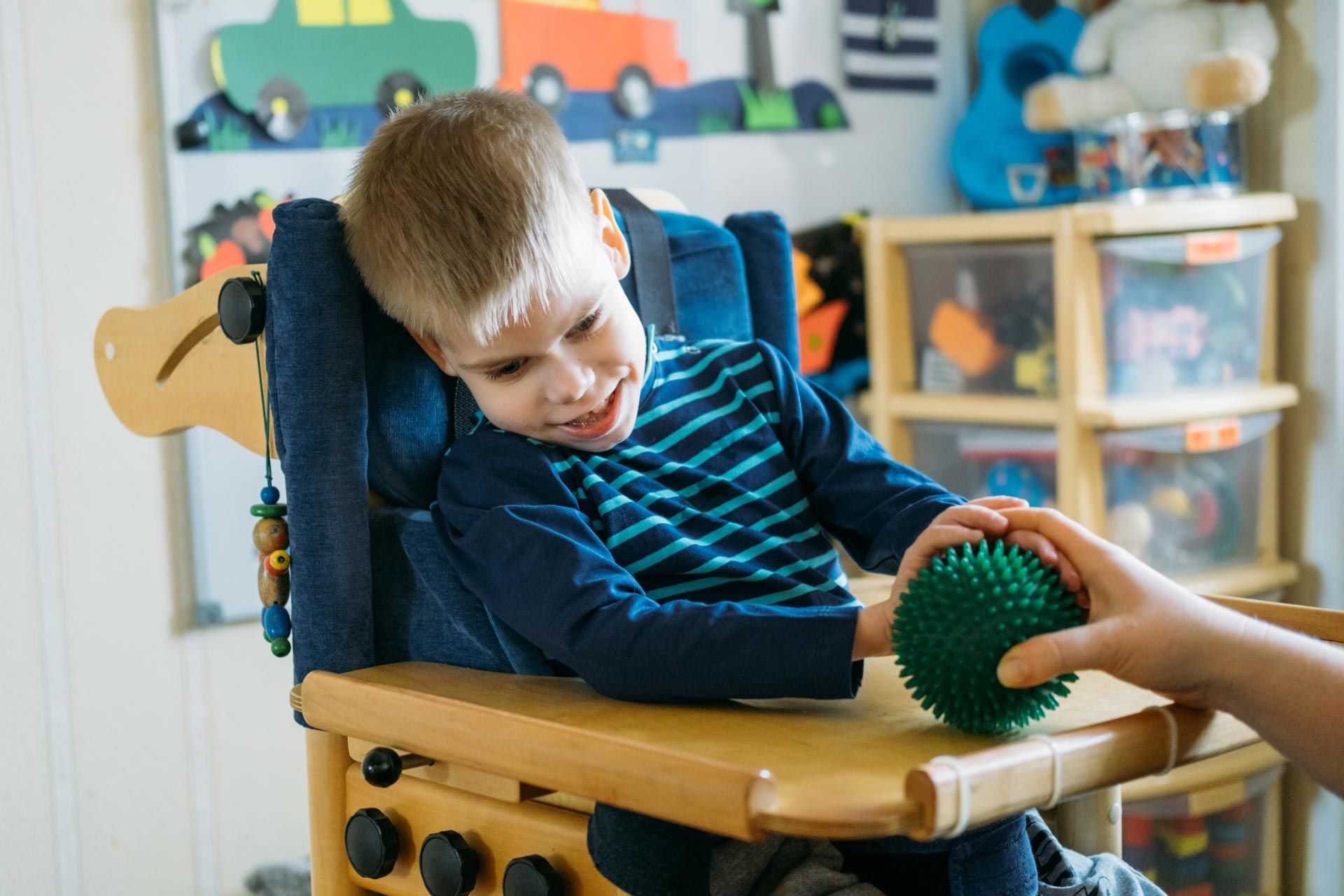 Young boy with CP wearing a blue and green striped shirt smiling playing with a sensory stress ball.