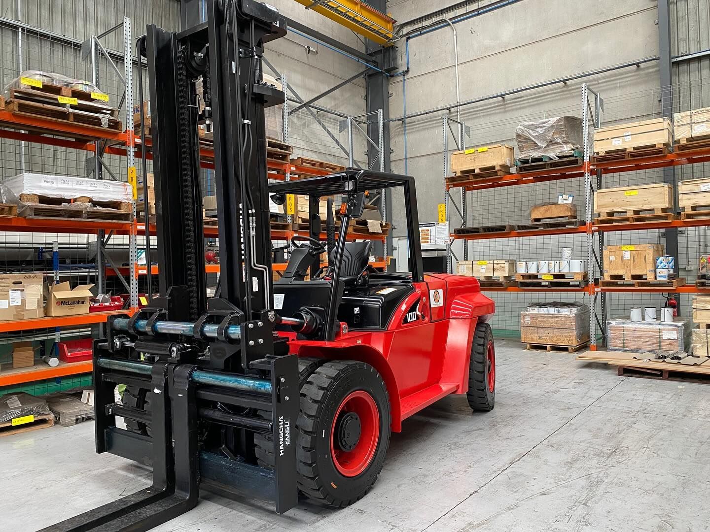 Red Forklift in a Warehouse Aisle Beside Stacked Pallets and Shelving — Lift It Equipment in Tuggerah, NSW