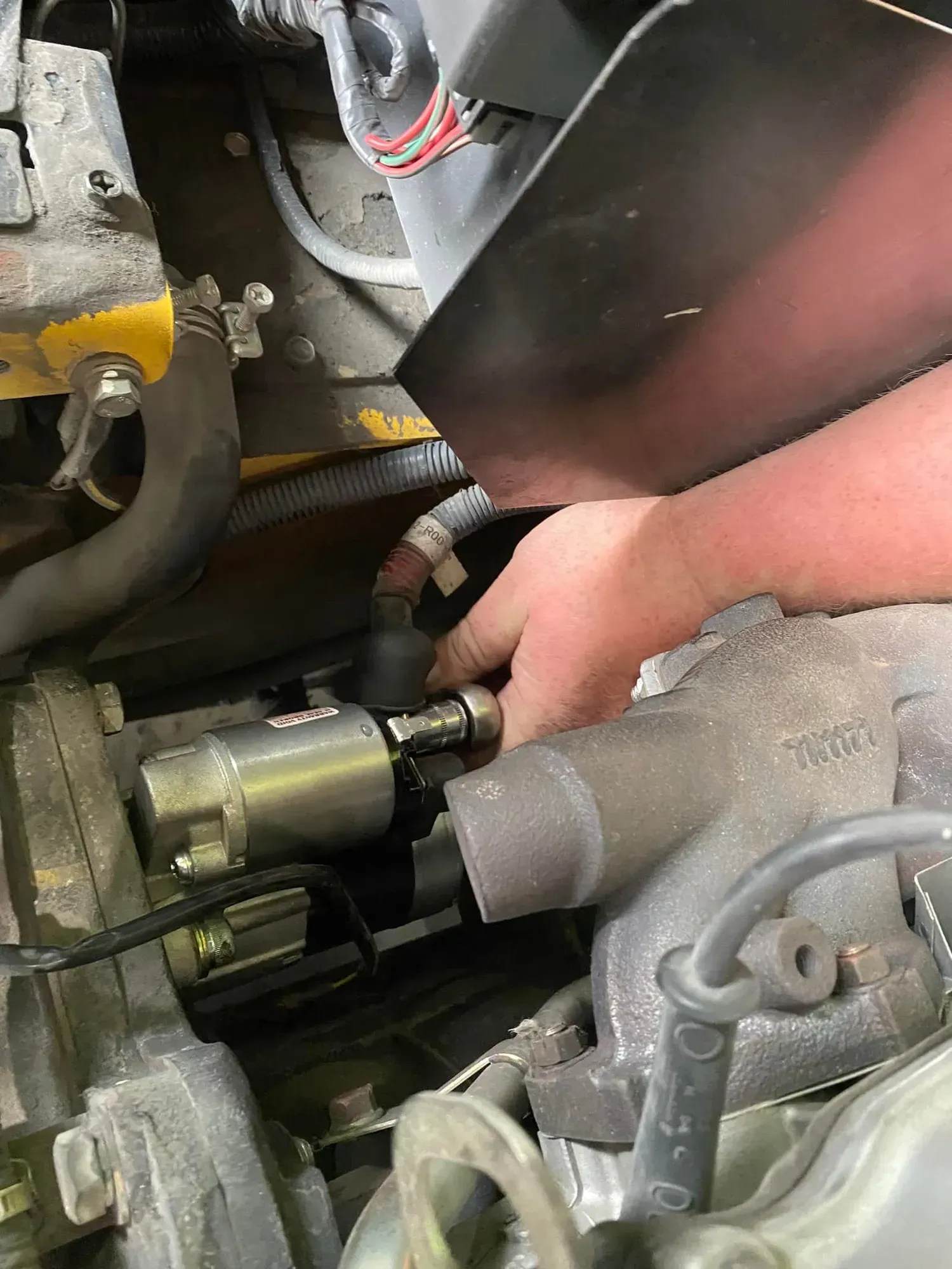 Hand Reaching Into a Car Engine Bay to Adjust a Metal Component — Lift It Equipment in Tuggerah, NSW