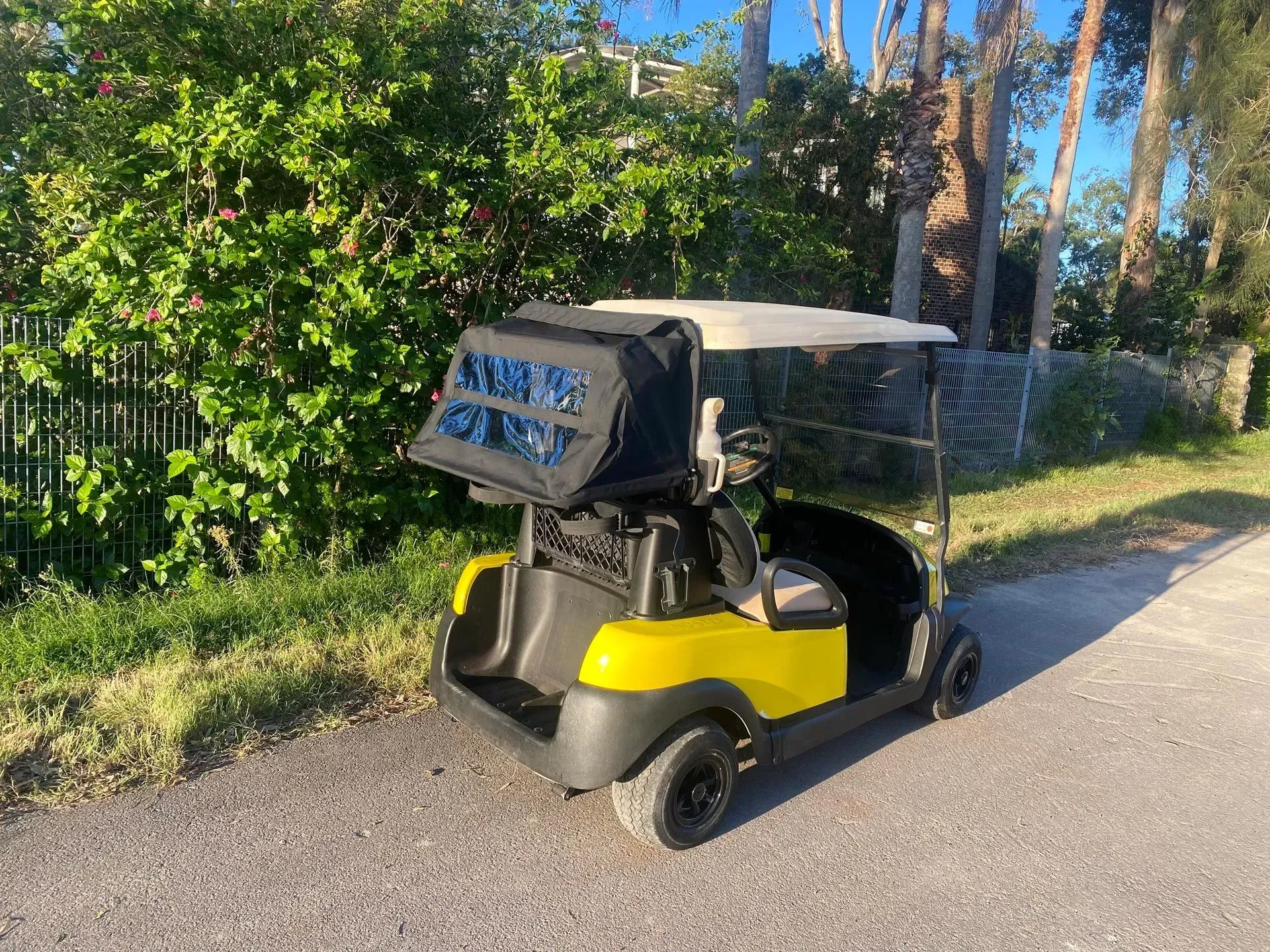 Yellow-and-black golf cart parked on a sunny roadside beside a chain-link fence and greenery — Lift It Equipment in Tuggerah, NSW