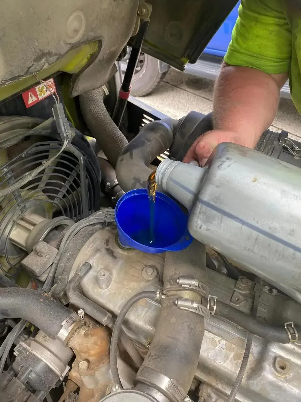 Mechanic Pouring Fluid Into a Blue Funnel in an Engine Bay — Lift It Equipment in Tuggerah, NSW