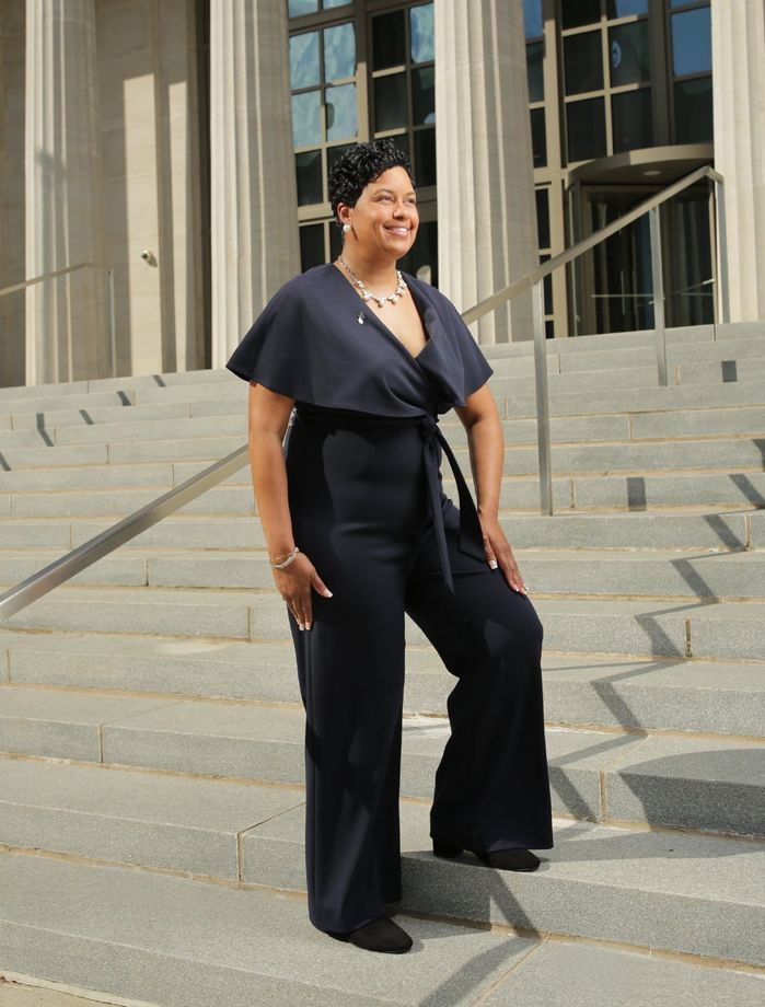 Person in a navy jumpsuit standing on stone steps outside a building.
