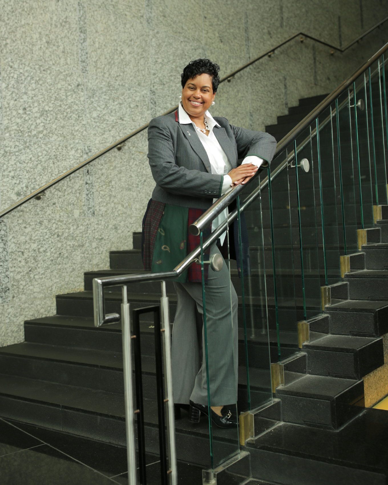 Woman in a gray suit leaning on a stair railing, smiling on a staircase.