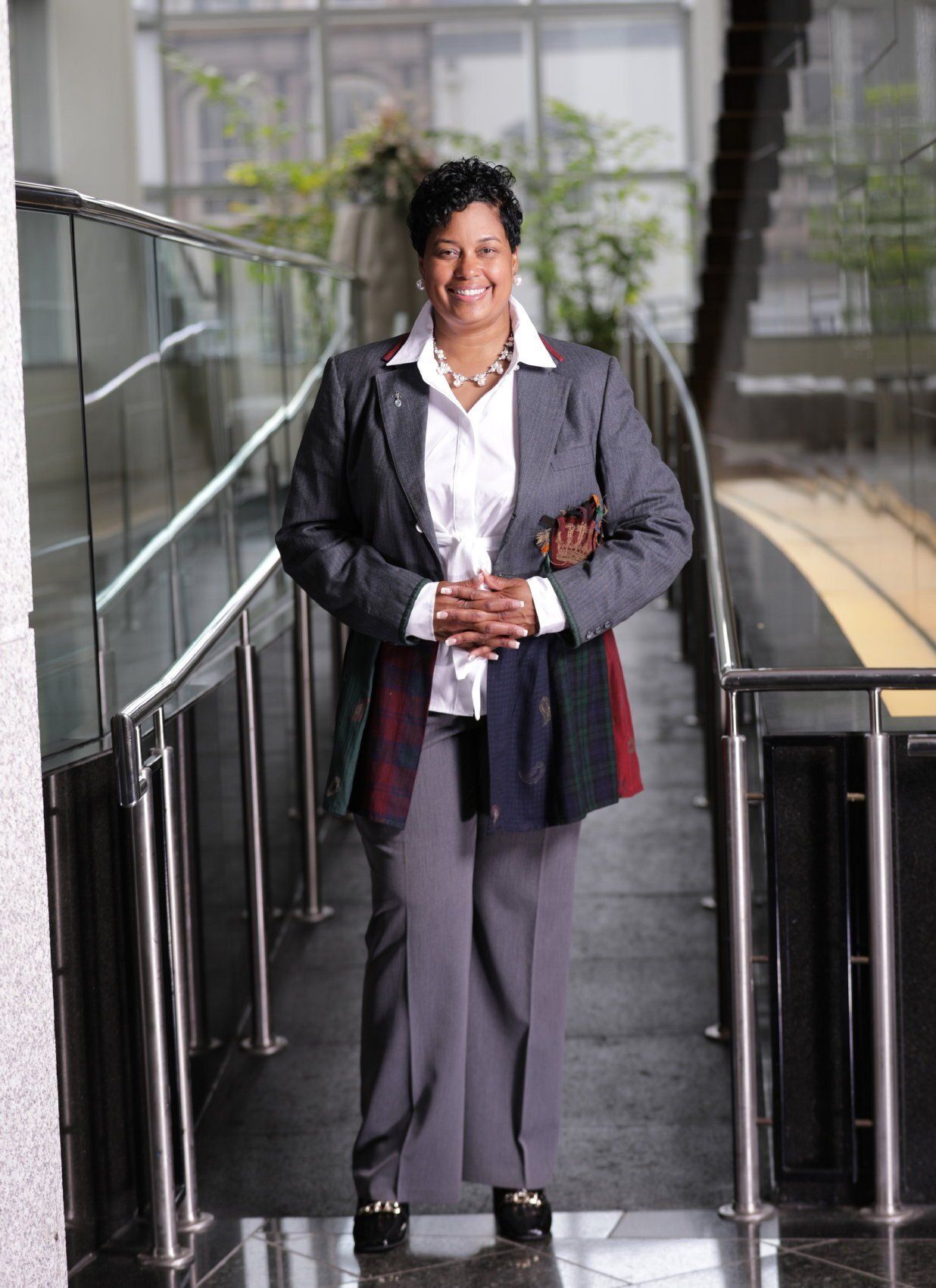 Person standing in a hallway, wearing a dark jacket and gray pants, holding papers.