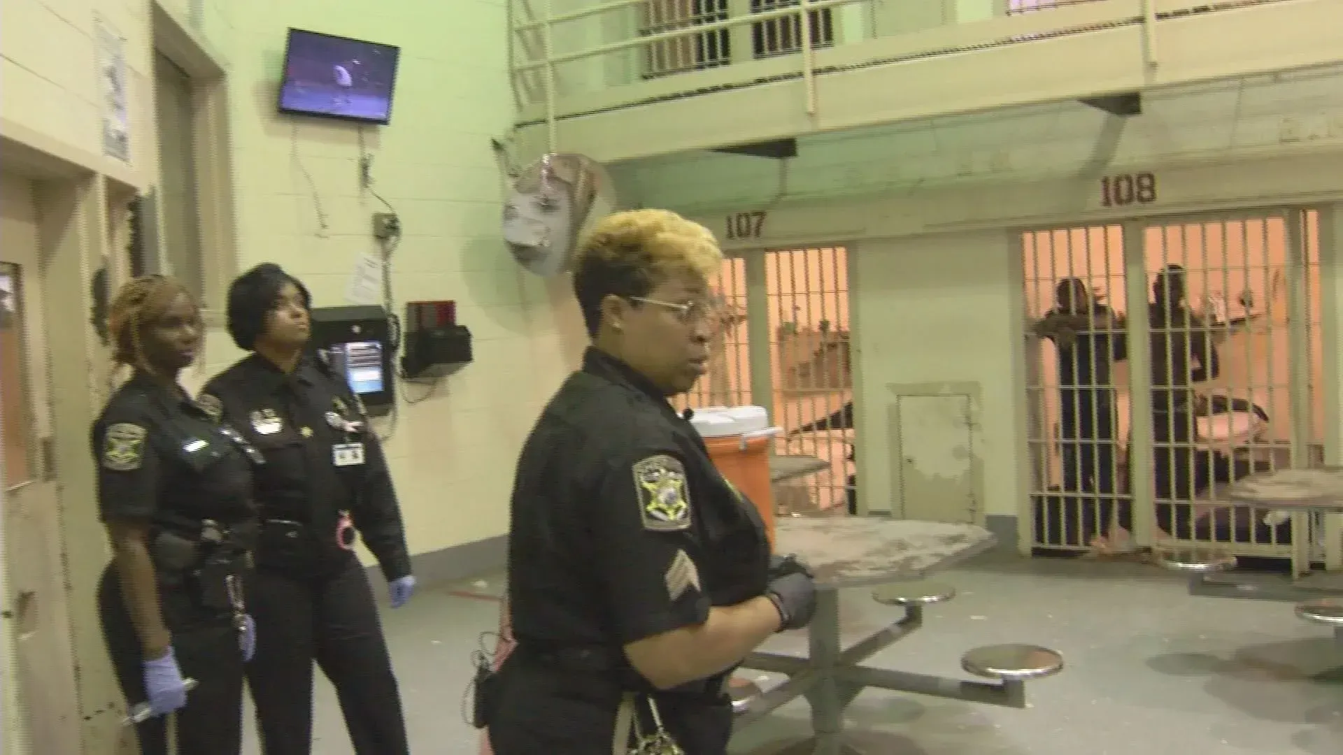 Police officers standing in a jail corridor near cell doors and barred windows
