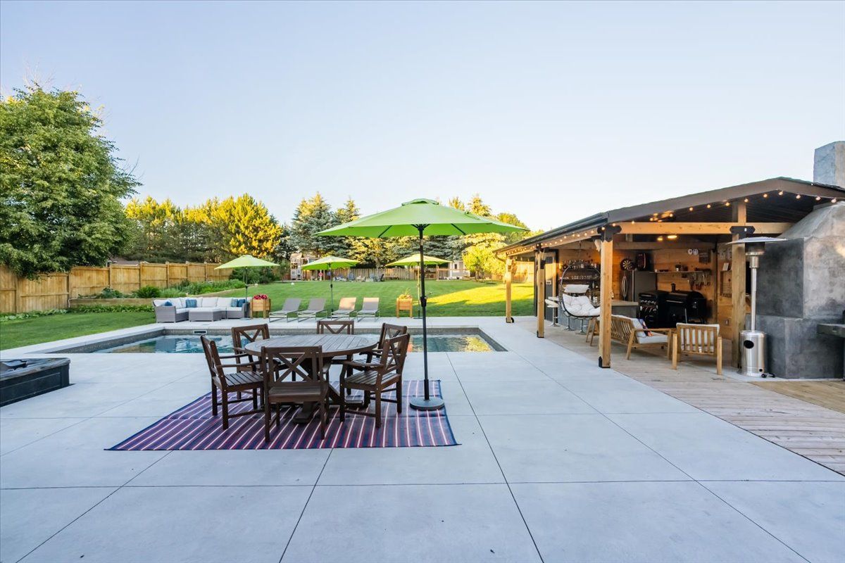 A patio with a table and chairs and umbrellas in front of a pool.