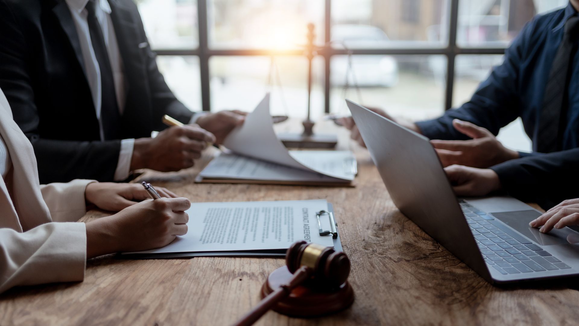 Three people in a meeting at a table, talking with documents in a bright office.
