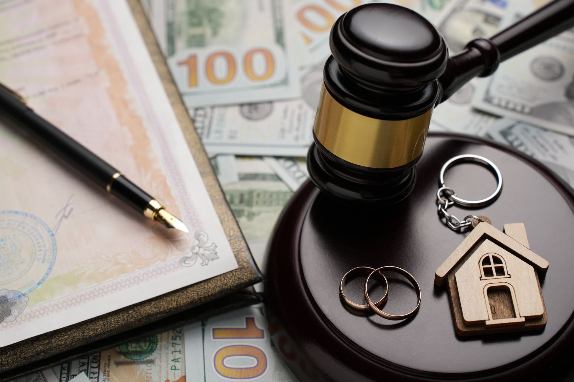Real estate contract with gavel, house keychain, rings, and pen on currency notes