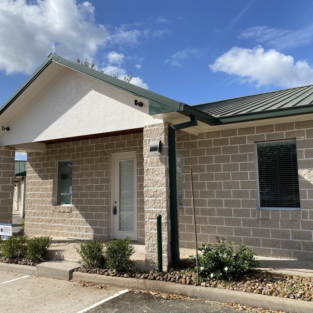 Exterior of a light brick building with green trim and a metal roof under a blue sky.