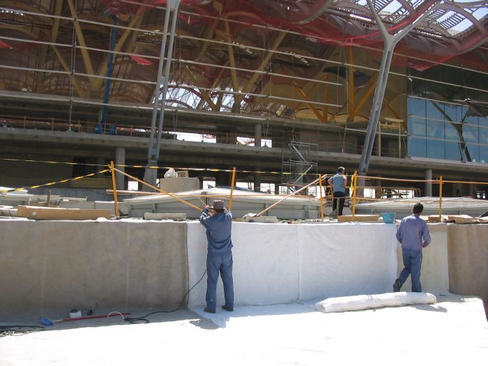 Obreros de la construcción en el interior de un gran edificio bajo vigas de acero, con un muro de hormigón en primer plano.