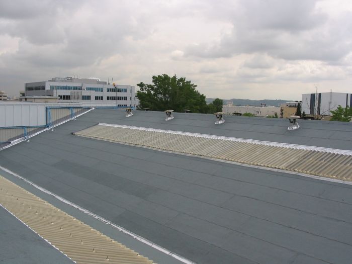 Azotea con techo gris bajo un cielo nublado, con edificios y árboles a lo lejos.