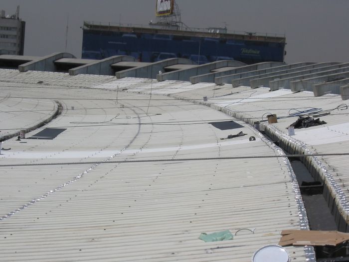 Azotea curva cubierta de nieve con paneles solares y un edificio al fondo.