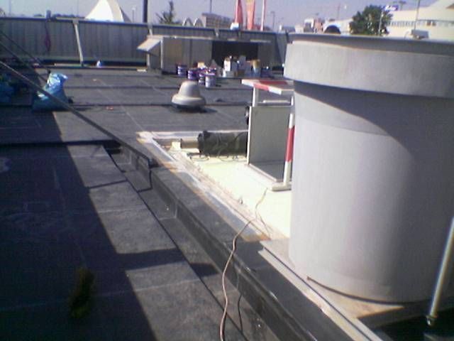 Azotea con grandes conductos de ventilación blancos, unidades de climatización y un horizonte urbano lejano bajo una luz clara.