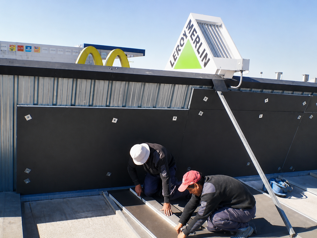 Dos trabajadores se agachan en una abertura en la azotea para instalar una trampilla debajo de un letrero de McDonald's.