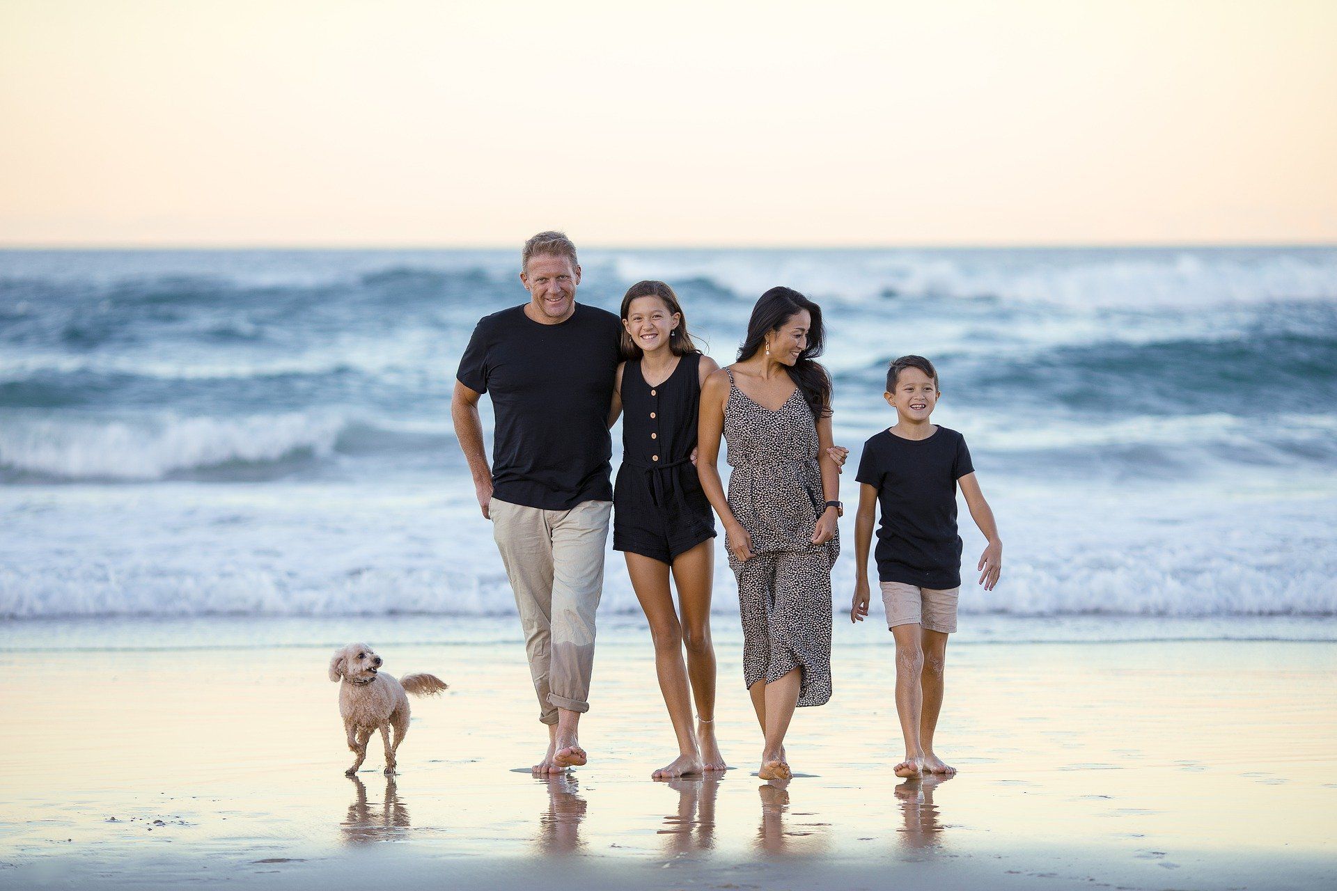 Family of four and dog walk on a beach at sunset.