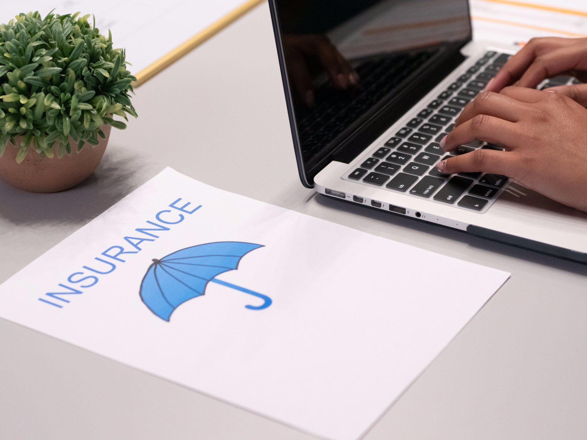 A person is typing on a laptop next to a piece of paper with an umbrella on it.