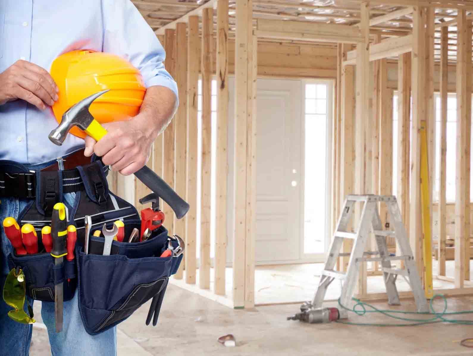 Ouvrier du bâtiment tenant un casque et un marteau à l'intérieur d'une maison à ossature bois