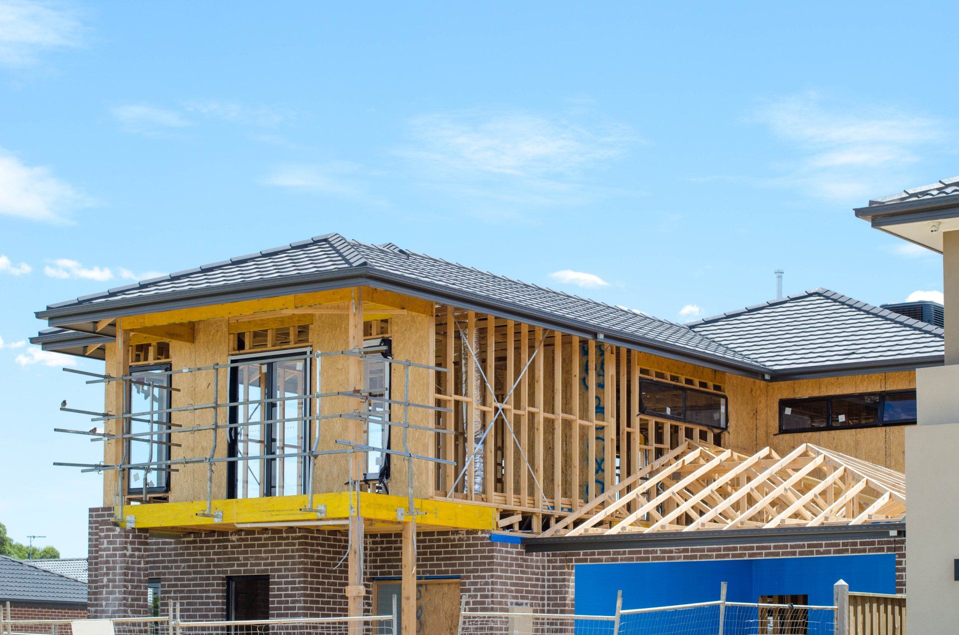 Maison en construction avec une ossature bois, des murs extérieurs jaunes et un ciel bleu au-dessus