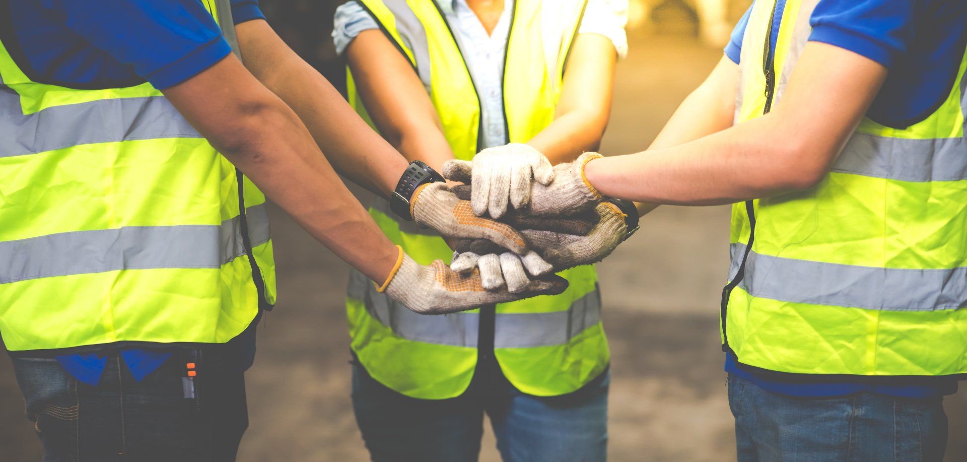 Des travailleurs portant des gilets de sécurité jaunes se tiennent la main en signe de travail d'équipe.