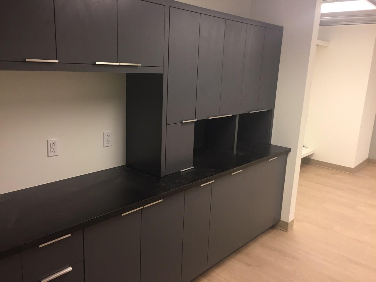 Des armoires de bureau encastrées sombres et un comptoir noir longent un mur dans une pièce vide.