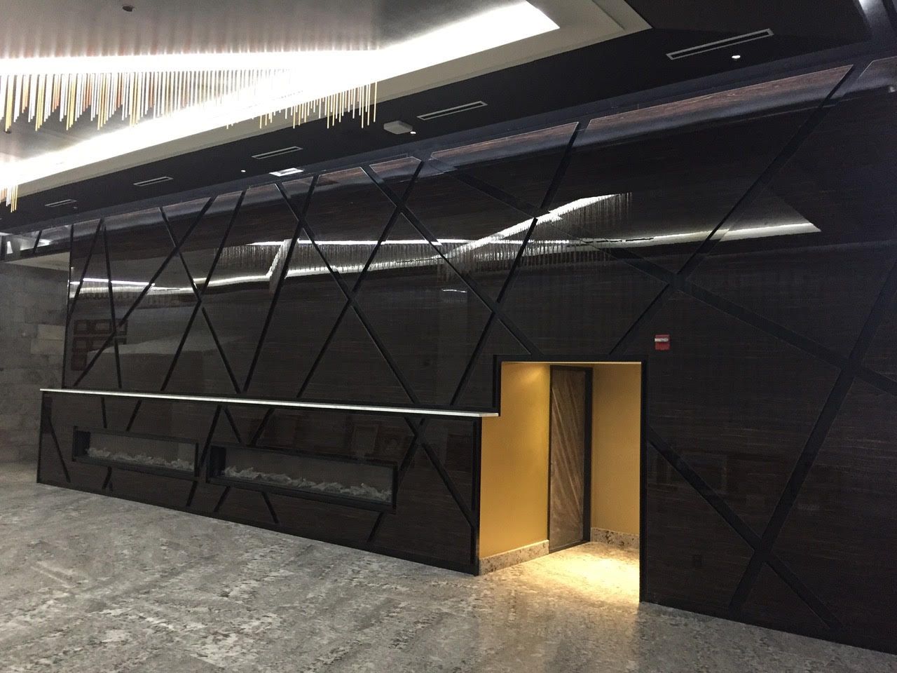 Intérieur de hall d'entrée moderne et noir avec panneaux muraux géométriques, luminaires suspendus et une porte ouverte éclairée chaleureusement.