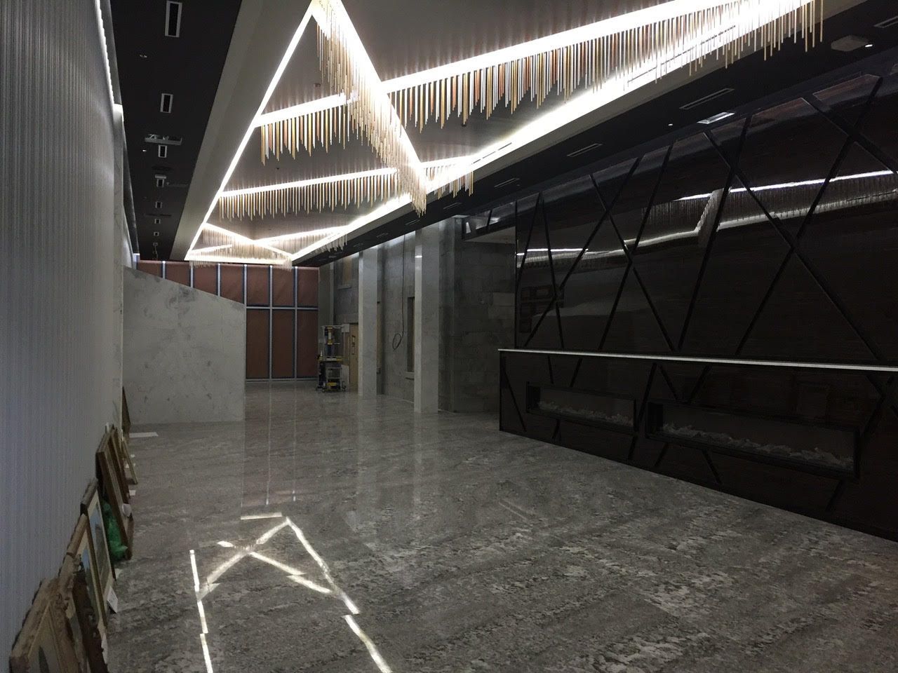Couloir moderne avec plafonniers LED géométriques, sol poli et reflets sur les murs en verre foncé.