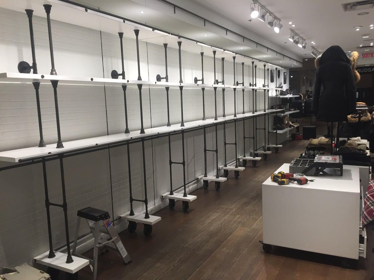Magasin de vêtements vide avec portants, étagères et comptoir d'exposition blanc sous une lumière vive