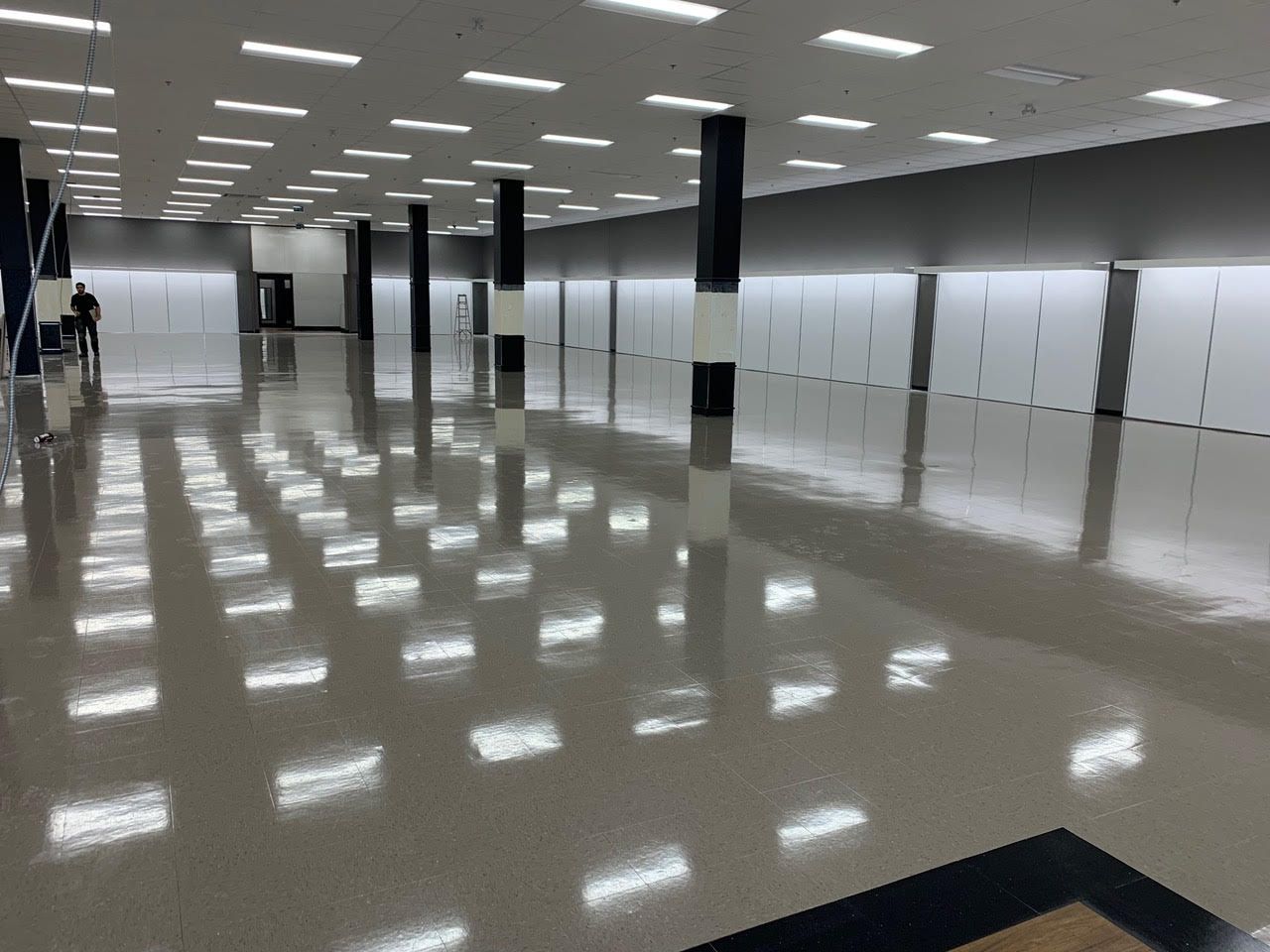 Couloir intérieur vide avec sol brillant, colonnes noires et panneaux muraux blancs reflétant la lumière du plafond