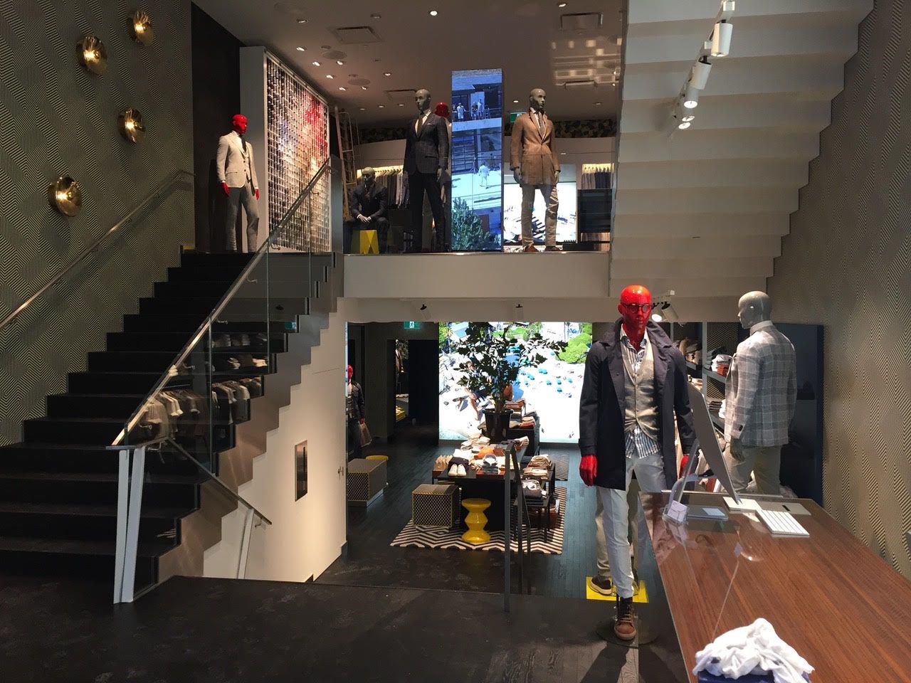 Intérieur d'un magasin de vêtements moderne avec des mannequins exposés et un escalier le long du mur de gauche.