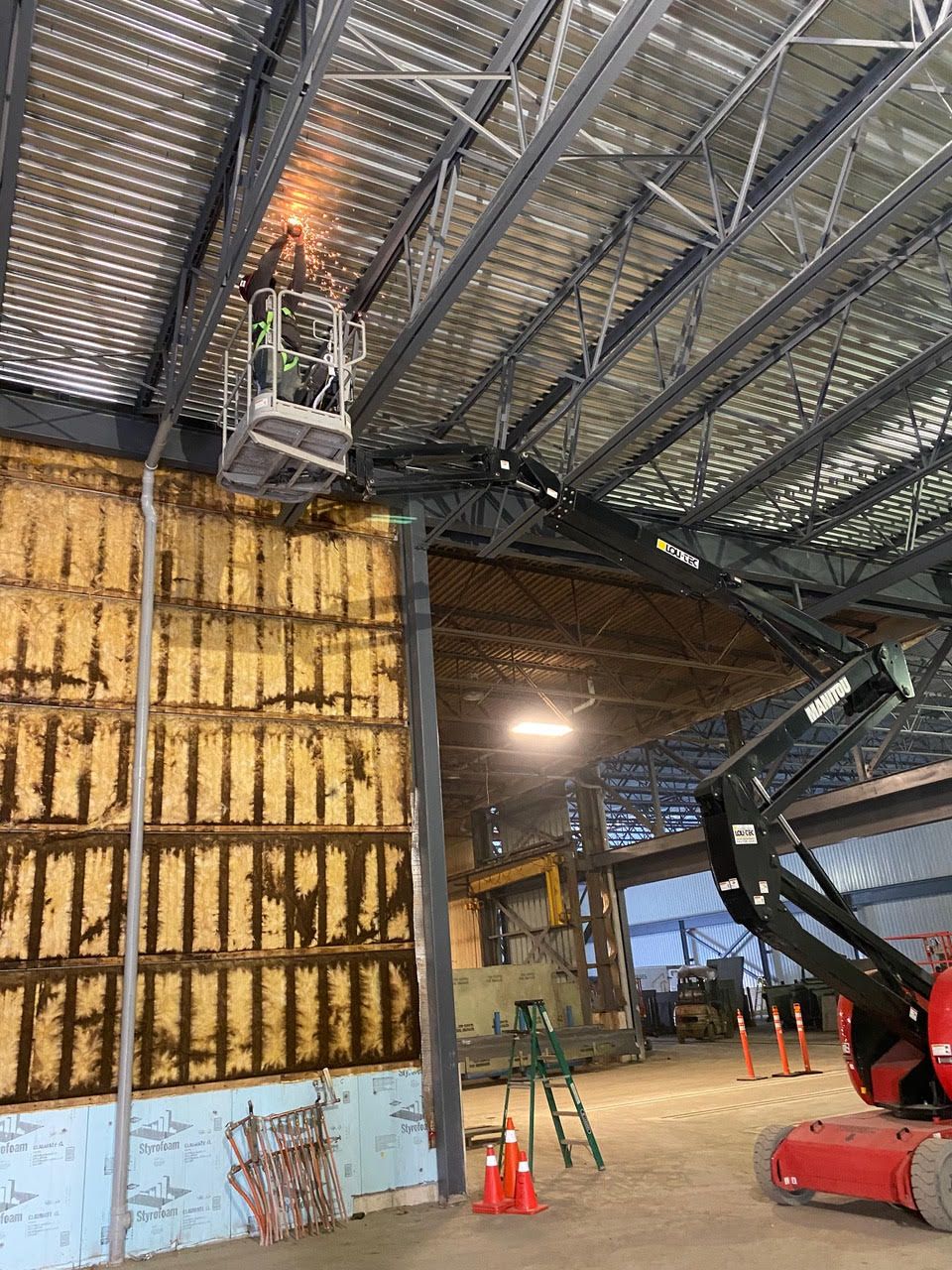 Intérieur d'un entrepôt industriel avec un ouvrier en hauteur près du plafond et un grand escalier sur la droite