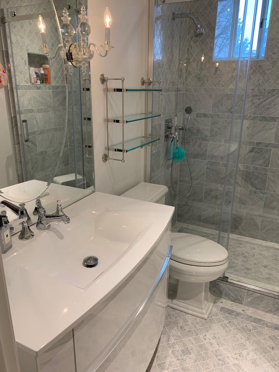 Salle de bains lumineuse carrelée avec douche en verre, lavabo blanc, toilettes et robinetterie chromée.