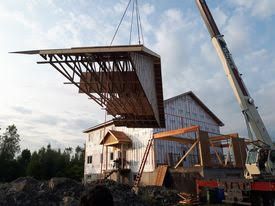 Maison en construction avec une grue soulevant une ferme de toit au coucher du soleil